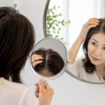 거울을 보며 가르마와 정수리의 갱년기 탈모 초기 변화를 확인하는 중년 여성