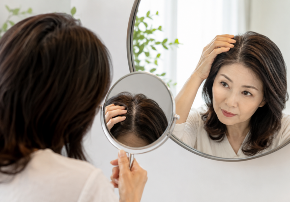 거울을 보며 가르마와 정수리의 갱년기 탈모 초기 변화를 확인하는 중년 여성